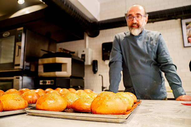 Baker removing freshly baked buns from oven