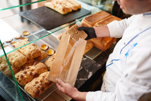Baker placing bread into a paper bag at bakery